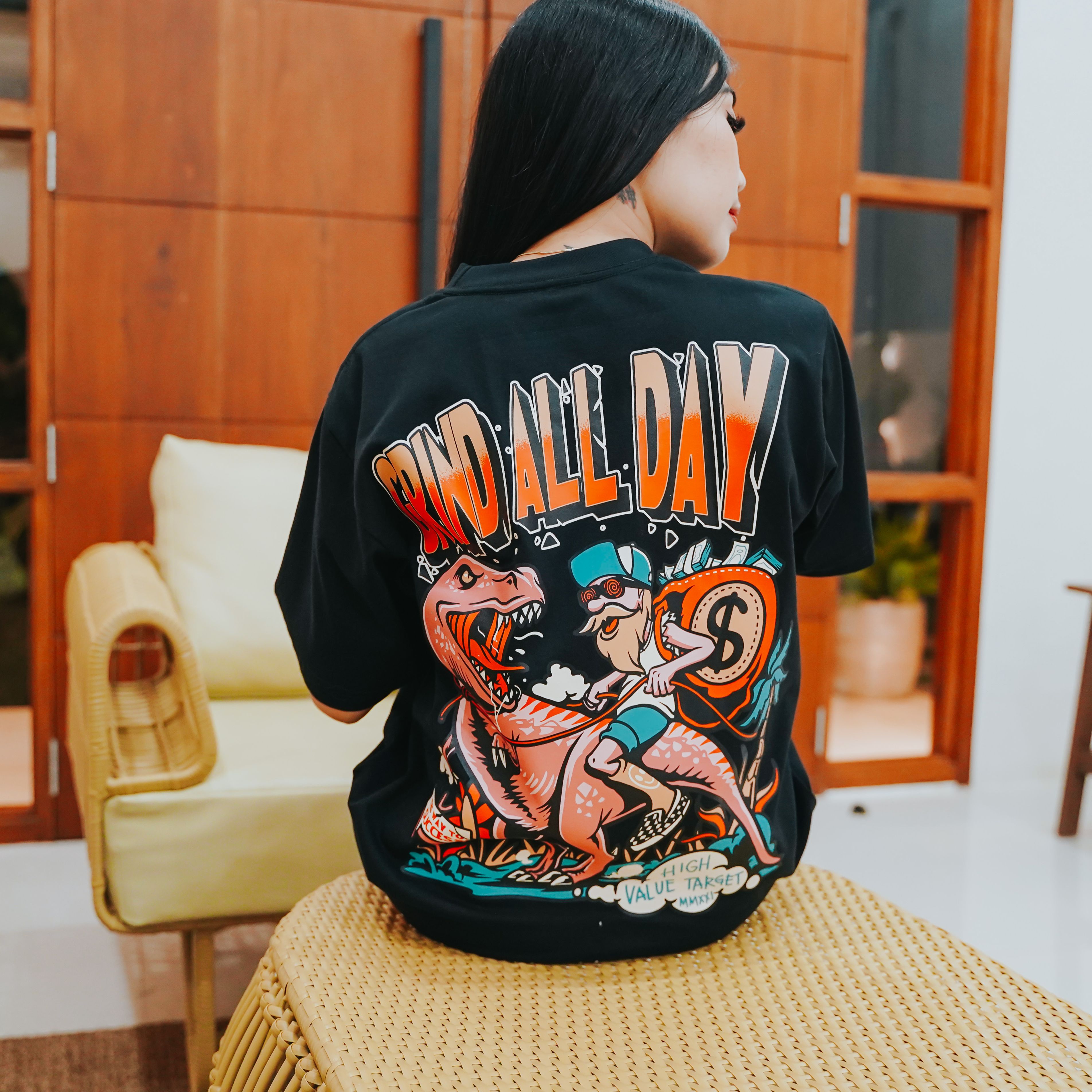 Graphic tee with dinosaur rider character and cash bag illustration with bold slogan