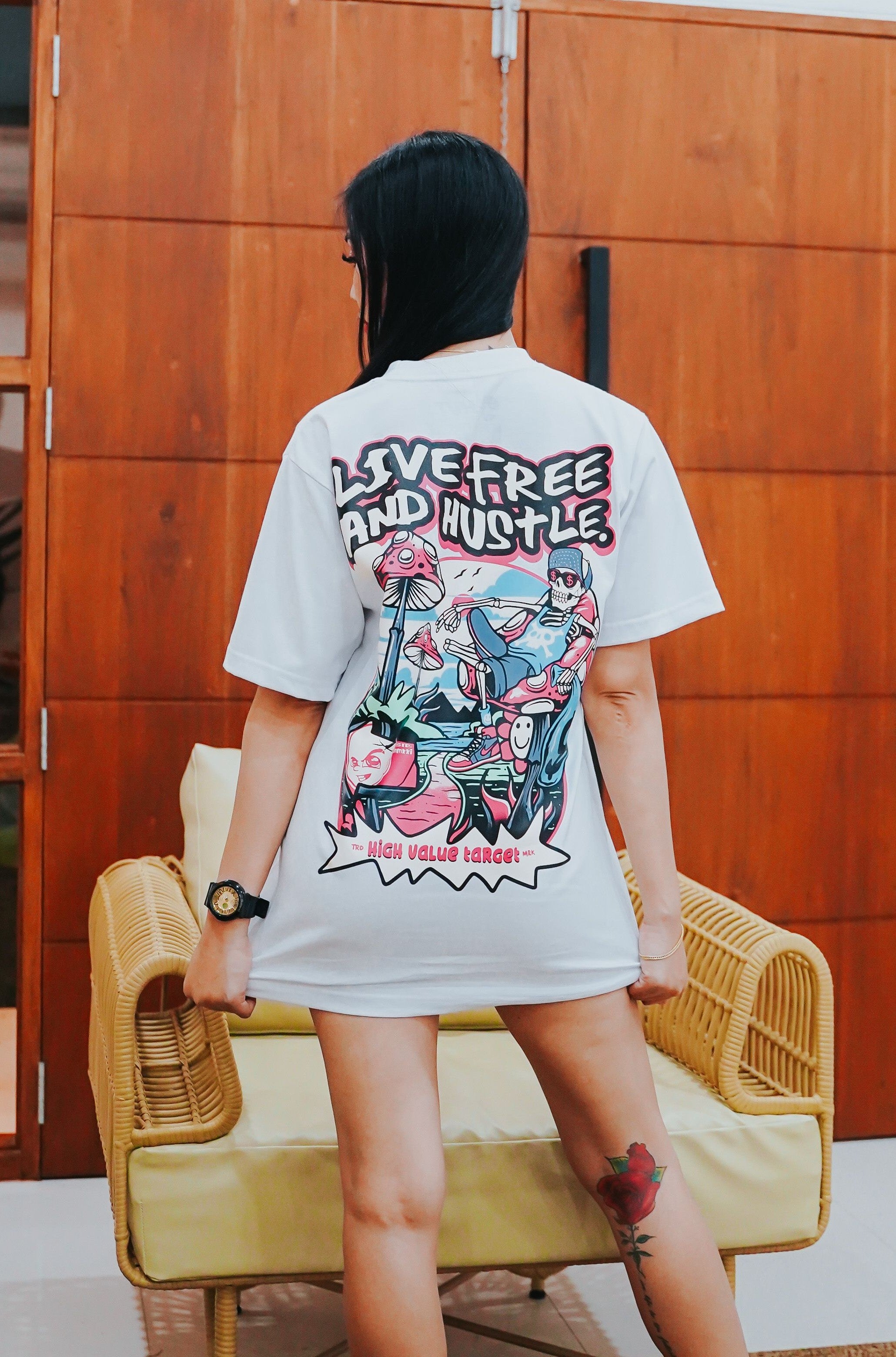 Graphic t-shirt featuring relaxed skeleton holding cash with mushrooms beside, Live Free and Hustle text streetwear design